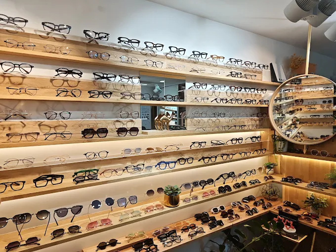 Le mur de montures d'Optique Squash, présentées sur des étagères de chêne clair éclairées.